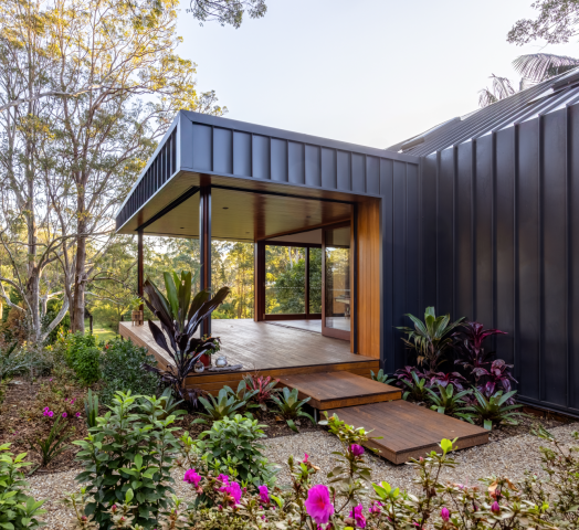 Contemporary home featuring LYSAGHT® ZENITH® range ENSEAM® cladding in a sleek dark finish, complemented by warm timber decking and large glass doors.