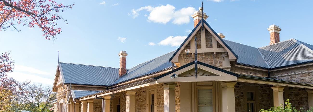 Heritage stone home with CUSTOM ORB® roofing, showcasing a blend of traditional architecture and modern roofing solutions under a sunny sky.