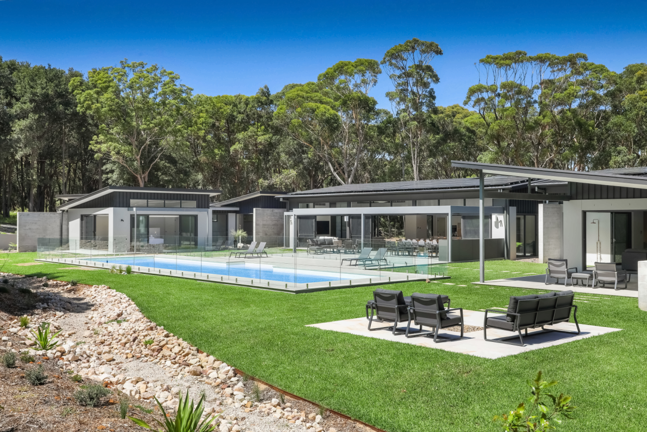 Modern luxury home featuring COLORBOND® steel in Monument color, with LYSAGHT® KLIP-LOK 700 HI-STRENGTH® roofing and ENSEAM® cladding. The property includes a sleek glass-fenced swimming pool, lush green lawn, and spacious outdoor entertaining areas with contemporary lounge seating.