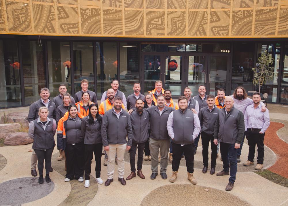 A diverse team in workwear and jackets poses outside a modern perforated building.